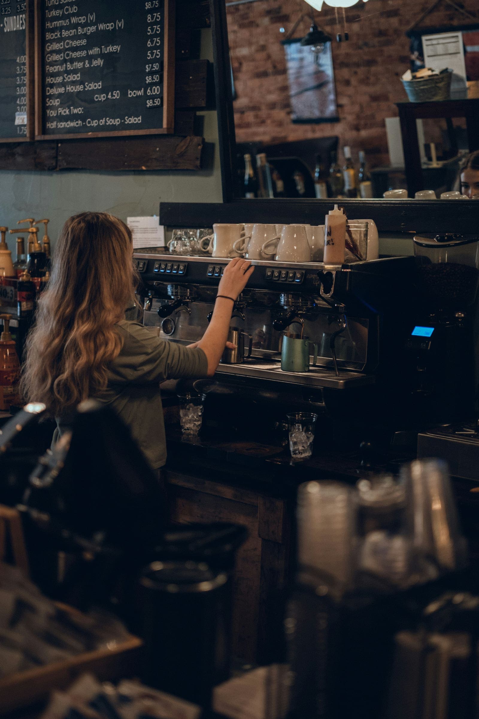 A barista pulling coffee at an espresso machine in a dim, warm café